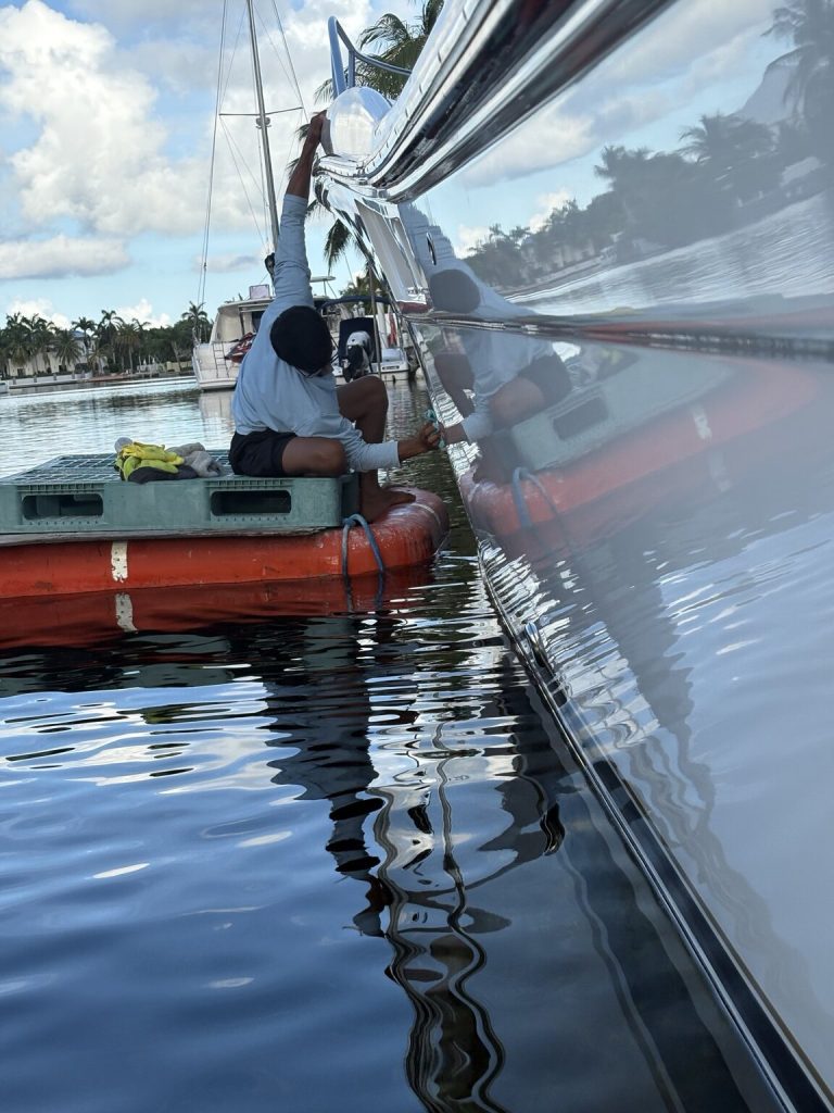 Detailer working from a floating platform beside the reflective Tiara hull on the water