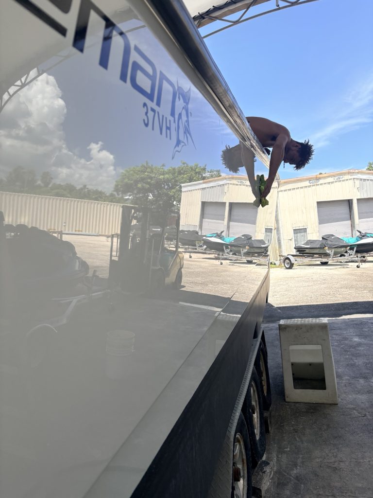 Detailer wiping the mirror-finish hull of a Freeman 37VH in the boatyard